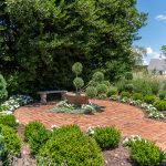 A beautiful red brick circular patio surrounding a lush green garden.