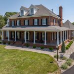 A beautiful luxurious red brick house with landscaping around the home of bushes and plants and river rock.