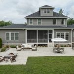 A beautiful luxury home with vinyl siding and a stone patio with a fire pit and outdoor stone grill.