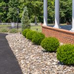 A close up of river rock and bushes - landscaping around the side of a red brick home.