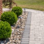 Close up of a grey stone pathway with a flower bed and river rock beside it.